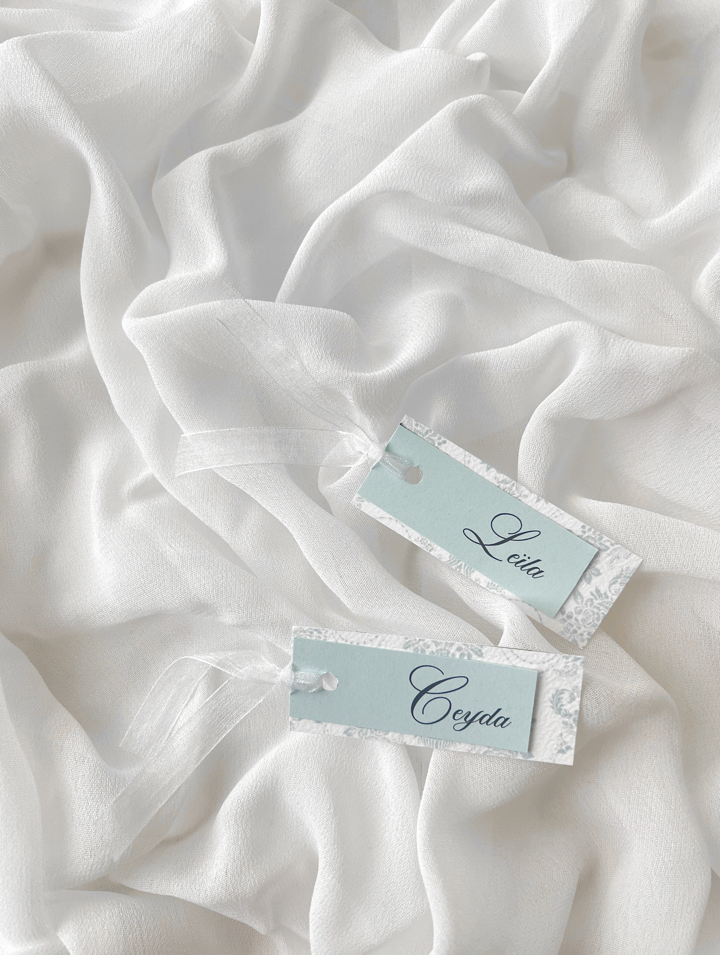 Marque-place de mariage personnalisé Collection WISTERIA II composé d'une carte florale bleu pastel clair et d'une carte supérieure colorée avec prénom personnalisé, disponible avec ou sans ruban ou gland.