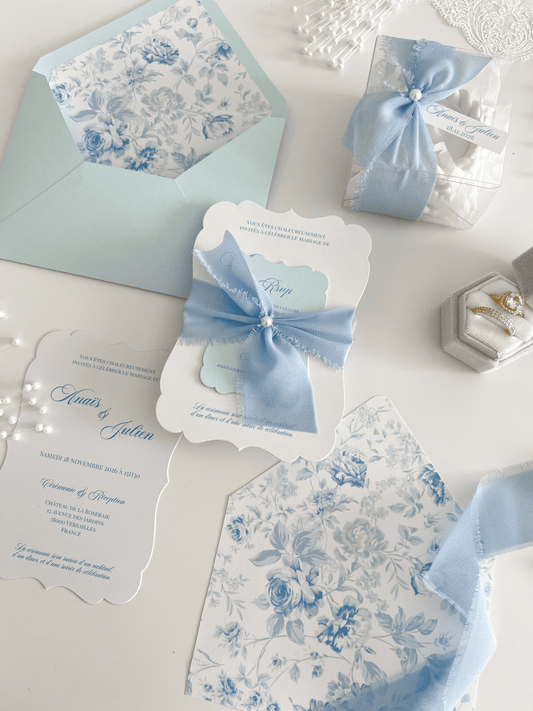 Faire-part de mariage personnalisé Collection LEA avec enveloppe bleu clair, liner floral bleu et blanc, découpe antique, ruban en mousseline de soie et carte RSVP assortie.