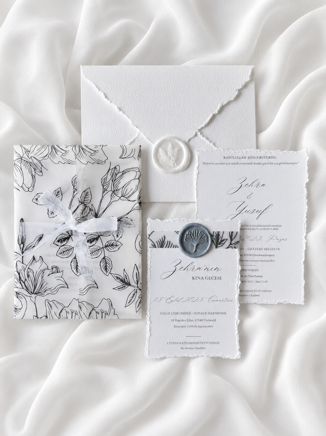 Faire-part de mariage personnalisé Collection CAMÉLIA avec enveloppe blanche effet déchiré, pochette vellum imprimée florale, cachet de cire blanc, ruban organza et carte RSVP assortie.
