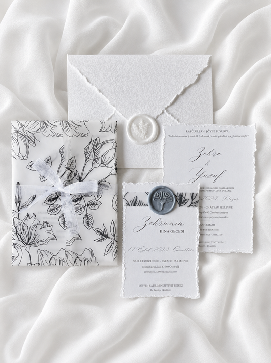 Faire-part de mariage personnalisé Collection CAMÉLIA avec enveloppe blanche effet déchiré, pochette vellum imprimée florale, cachet de cire blanc, ruban organza et carte RSVP assortie.