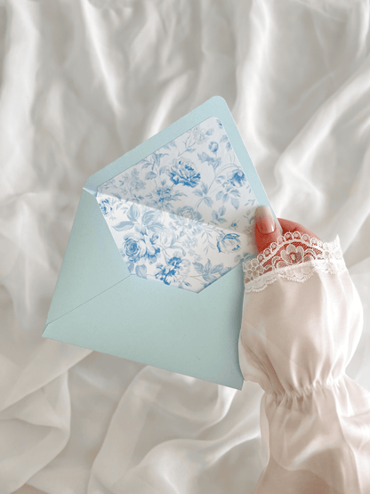 Faire-part de mariage personnalisé Collection LEA avec enveloppe bleu clair, liner floral bleu et blanc, découpe antique, ruban en mousseline de soie et carte RSVP assortie.
