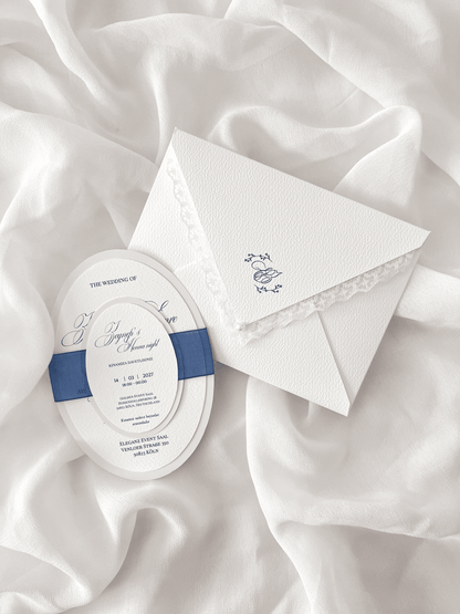 Faire-part de mariage personnalisé Collection MONARCH avec enveloppe blanche à contour dentelle, liner intérieur avec monogramme, invitation ovale doublée, carte RSVP assortie et large ruban bleu foncé.