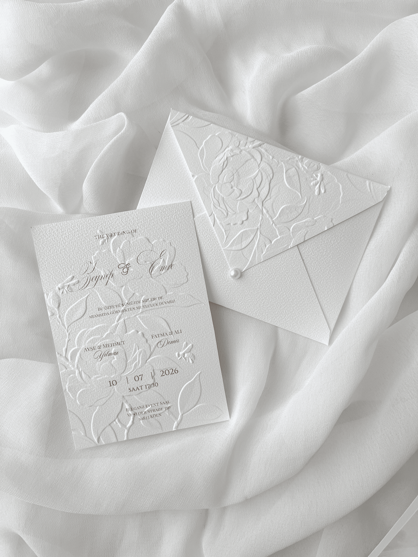 Faire-part de mariage personnalisé Collection PEONY avec enveloppe blanche embossée de motifs pivoines, invitation assortie avec embossage floral, perle décorative et carte RSVP en option.