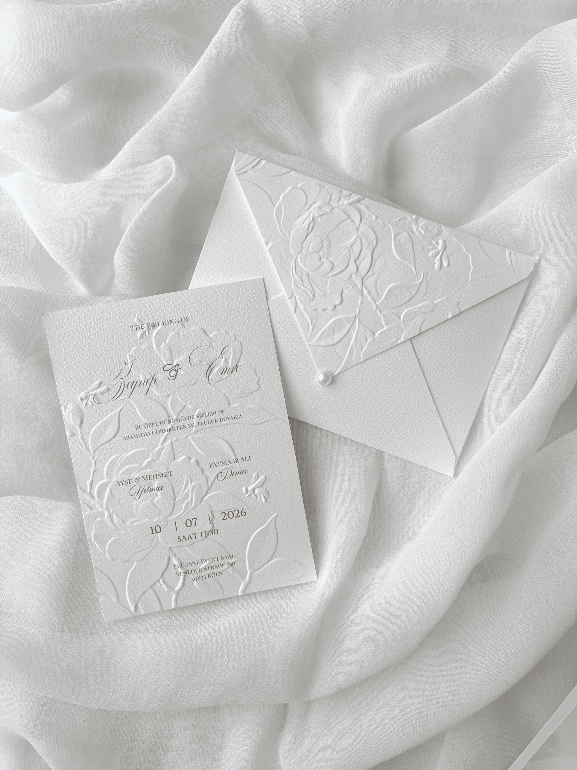 Faire-part de mariage personnalisé Collection PEONY avec enveloppe blanche embossée de motifs pivoines, invitation assortie avec embossage floral, perle décorative et carte RSVP en option.