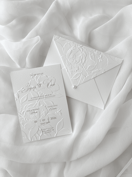 Faire-part de mariage personnalisé Collection PEONY avec enveloppe blanche embossée de motifs pivoines, invitation assortie avec embossage floral, perle décorative et carte RSVP en option.