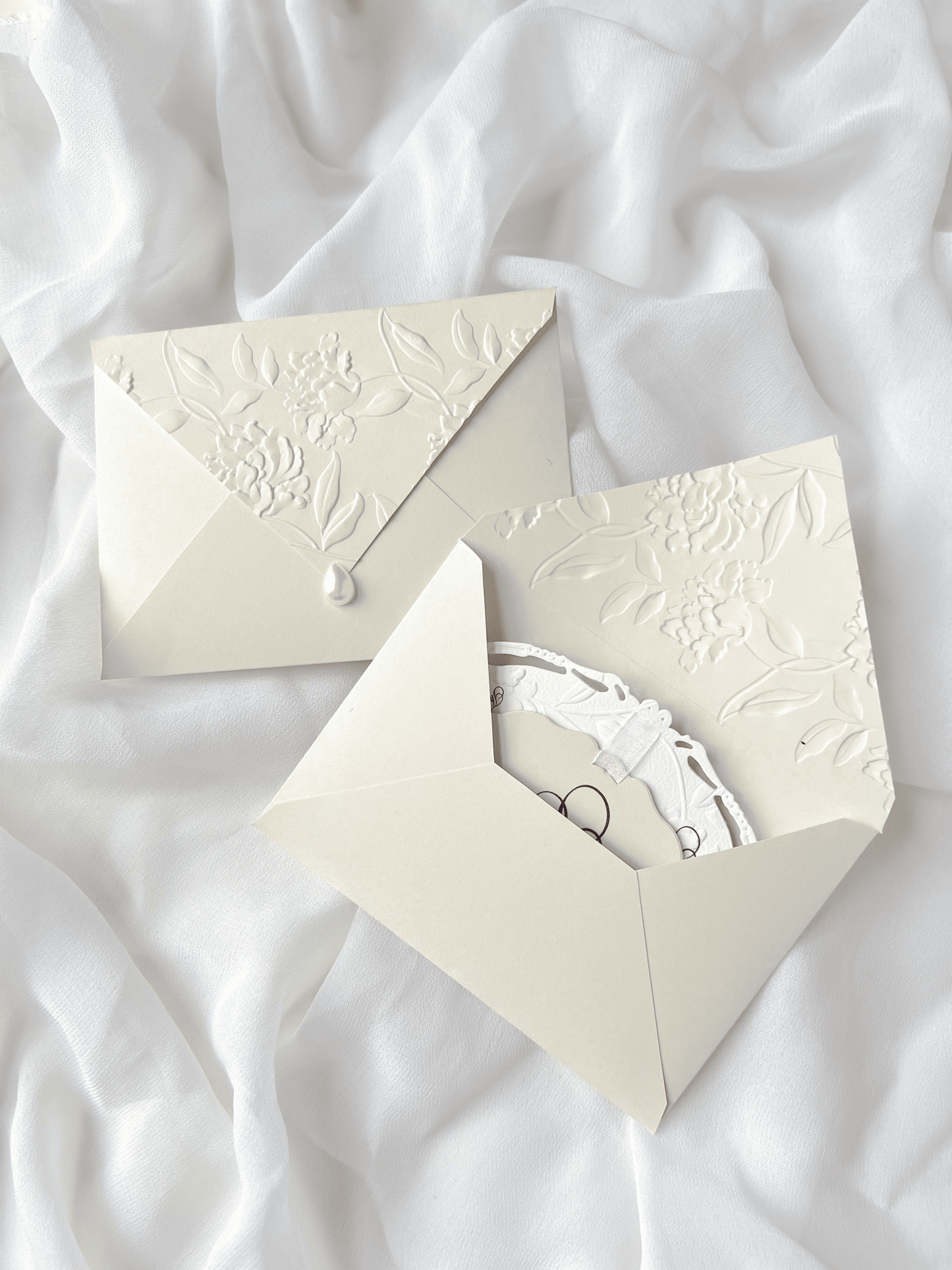 Faire-part de mariage personnalisé Collection WINDSOR avec enveloppe grège embossée, invitation ovale ajourée, ruban en organza, perle décorative et carte RSVP avec monogramme.