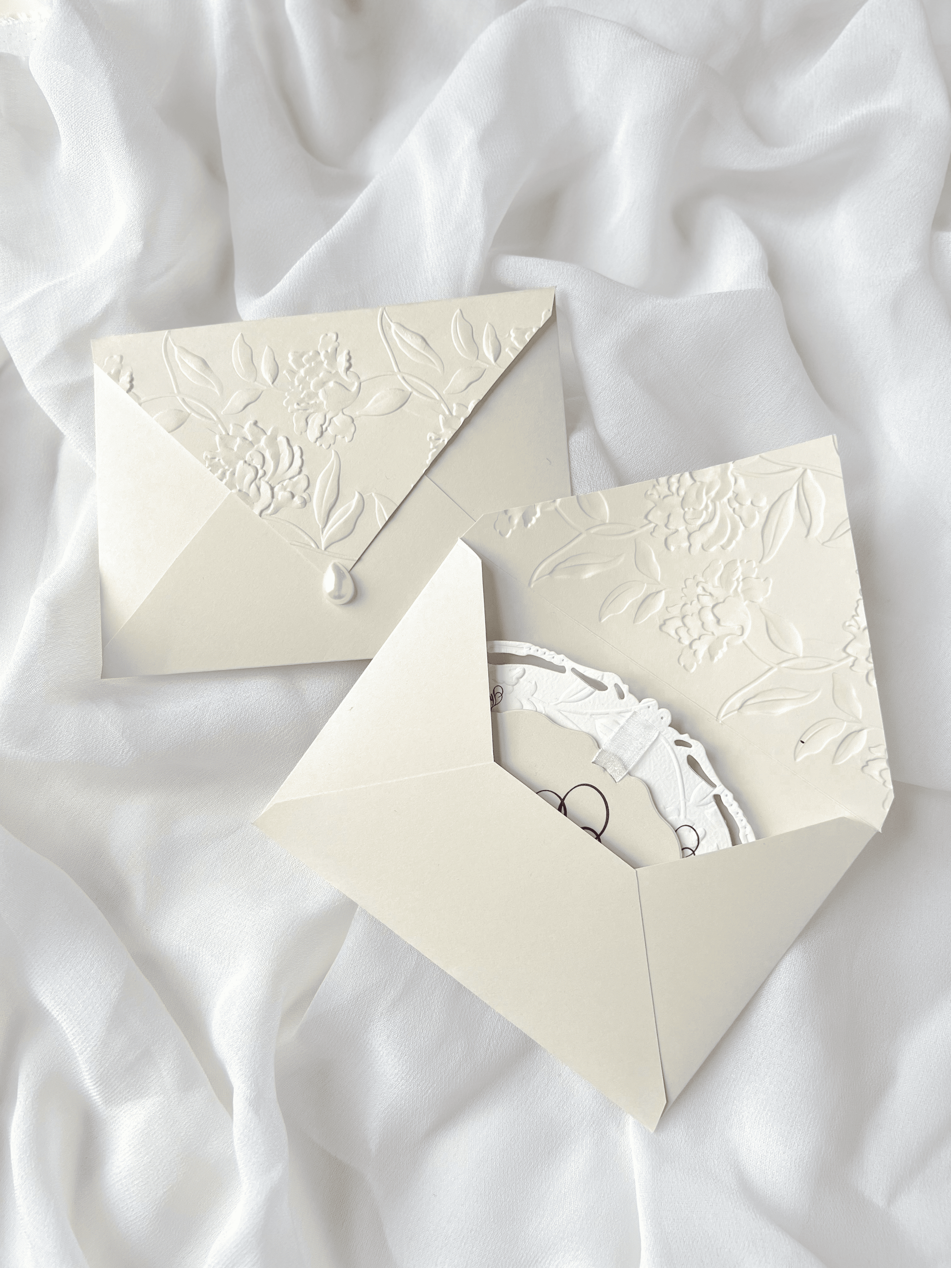 Faire-part de mariage personnalisé Collection WINDSOR avec enveloppe grège embossée, invitation ovale ajourée, ruban en organza, perle décorative et carte RSVP avec monogramme.