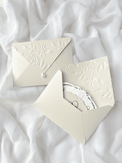 Faire-part de mariage personnalisé Collection WINDSOR avec enveloppe grège embossée, invitation ovale ajourée, ruban en organza, perle décorative et carte RSVP avec monogramme.