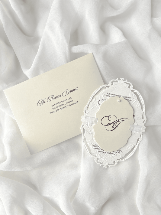 Faire-part de mariage personnalisé Collection WINDSOR avec enveloppe grège embossée, invitation ovale ajourée, ruban en organza, perle décorative et carte RSVP avec monogramme.