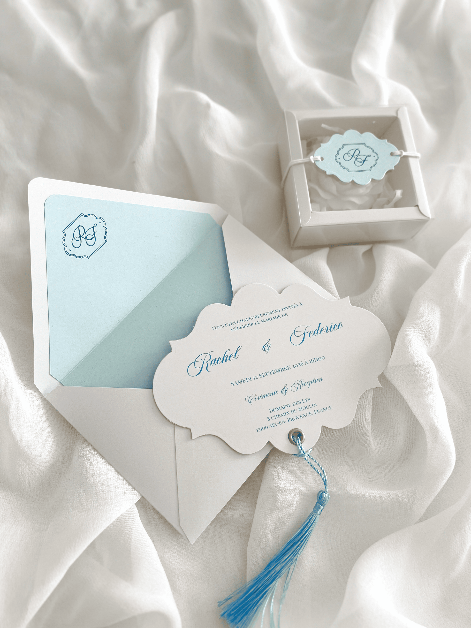 Faire-part de mariage personnalisé Collection RACHEL avec enveloppe blanche, liner bleu clair personnalisé avec monogramme, découpe impériale, gland bleu et carte RSVP assortie.