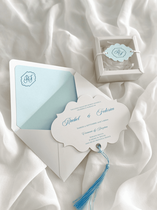 Faire-part de mariage personnalisé Collection RACHEL avec enveloppe blanche, liner bleu clair personnalisé avec monogramme, découpe impériale, gland bleu et carte RSVP assortie.