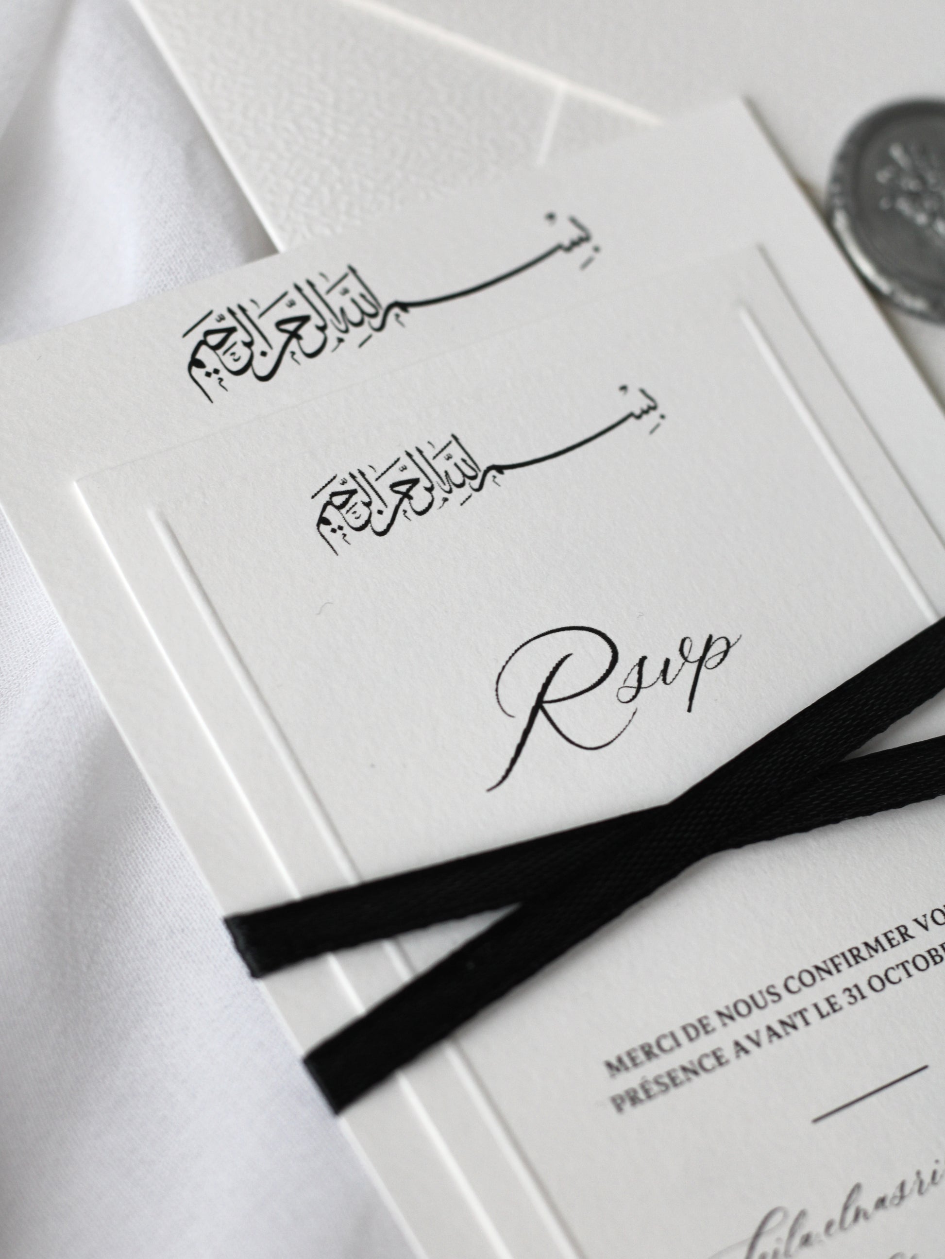 Faire-part de mariage personnalisé Collection SIGNATURE avec enveloppe blanche, cachet de cire, invitation ornée d'un ruban noir croisé et carte RSVP à contour embossé en option.
