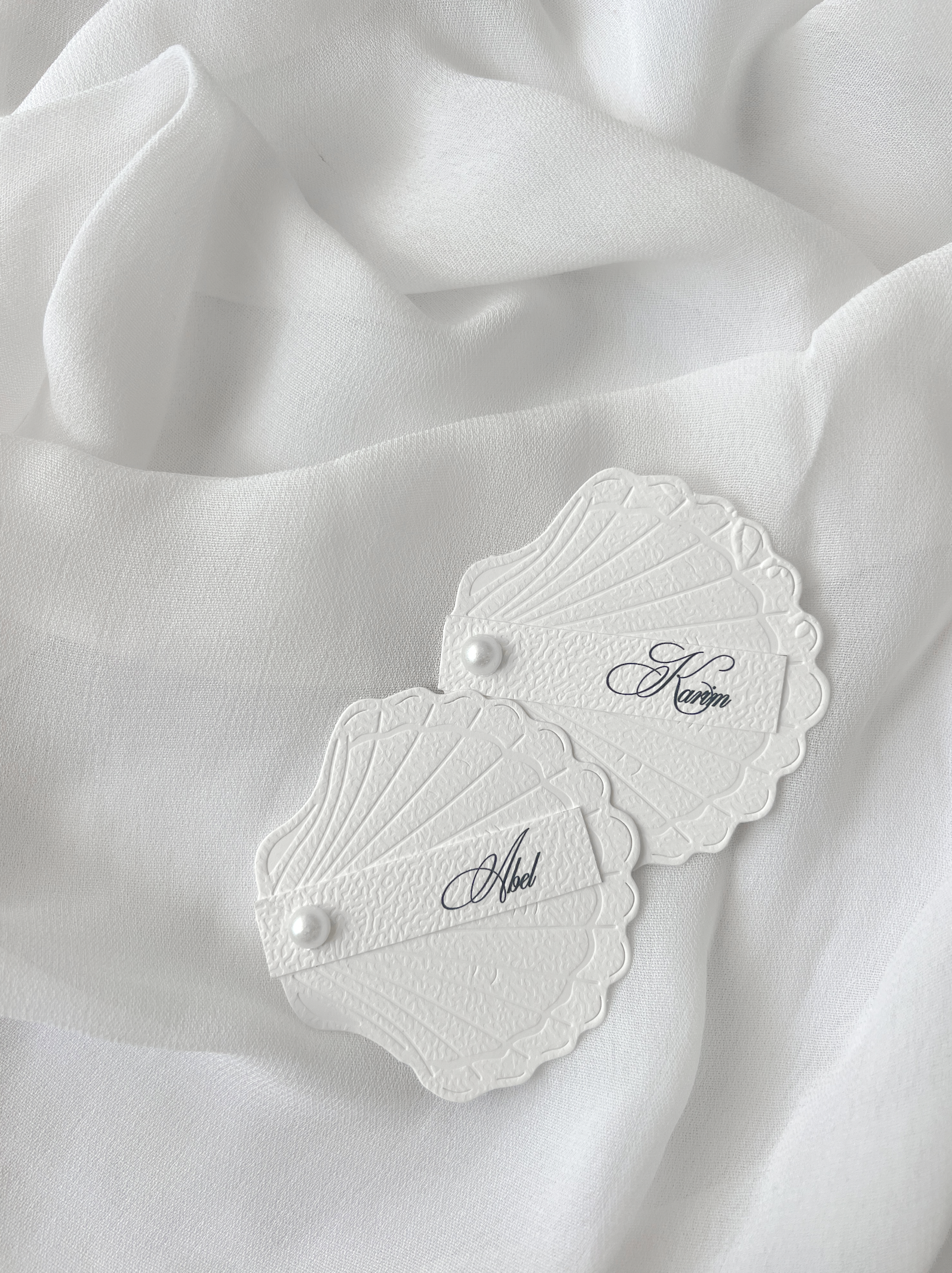 Marque-place de mariage personnalisé Collection SHELL II en forme de coquillage avec carte prénom personnalisée et finition perle décorative.
