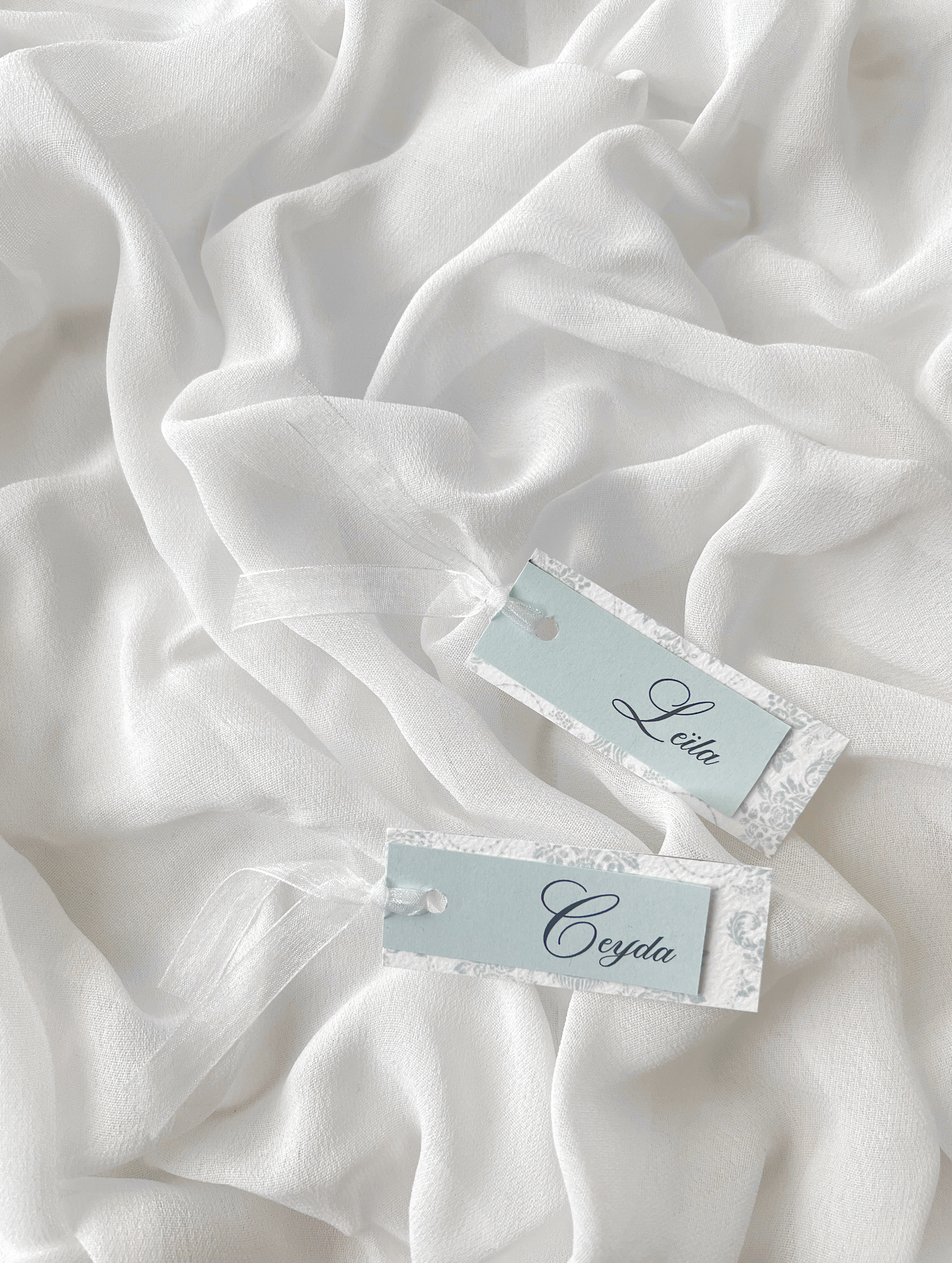 Marque-place de mariage personnalisé Collection WISTERIA II composé d'une carte florale bleu pastel clair et d'une carte supérieure colorée avec prénom personnalisé, disponible avec ou sans ruban ou gland.
