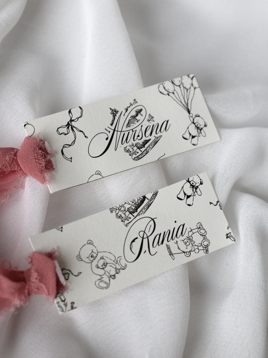 Marque-place personnalisé Collection MÉLODIE au format 10 × 4 cm avec adorable motif enfant, disponible avec ou sans ruban ou gland.