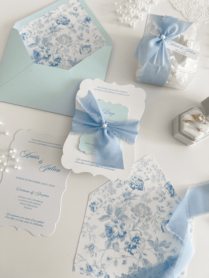 Faire-part de mariage personnalisé Collection LEA avec enveloppe bleu clair, liner floral bleu et blanc, découpe antique, ruban en mousseline de soie et carte RSVP assortie.
